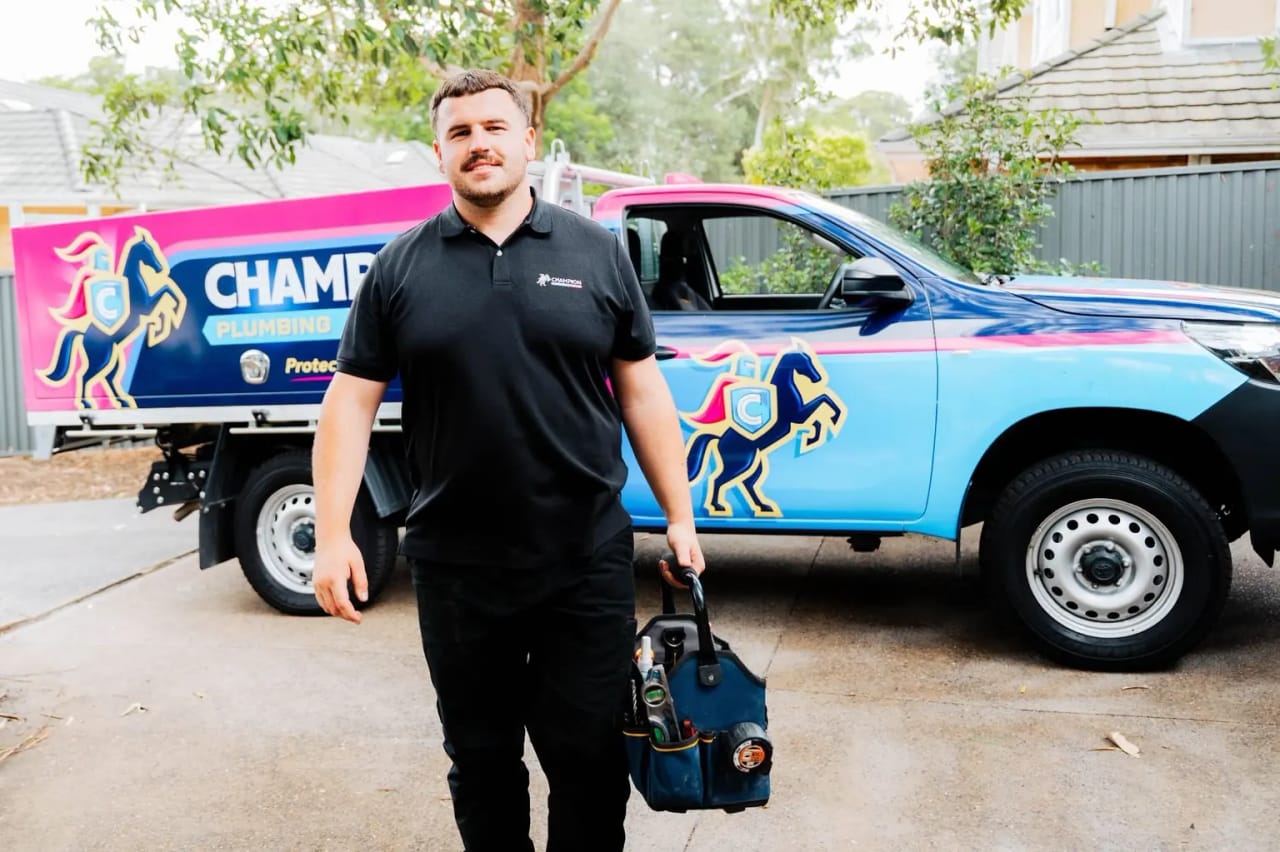 A Champion plumber with his toolbag in front of the Champion truck.